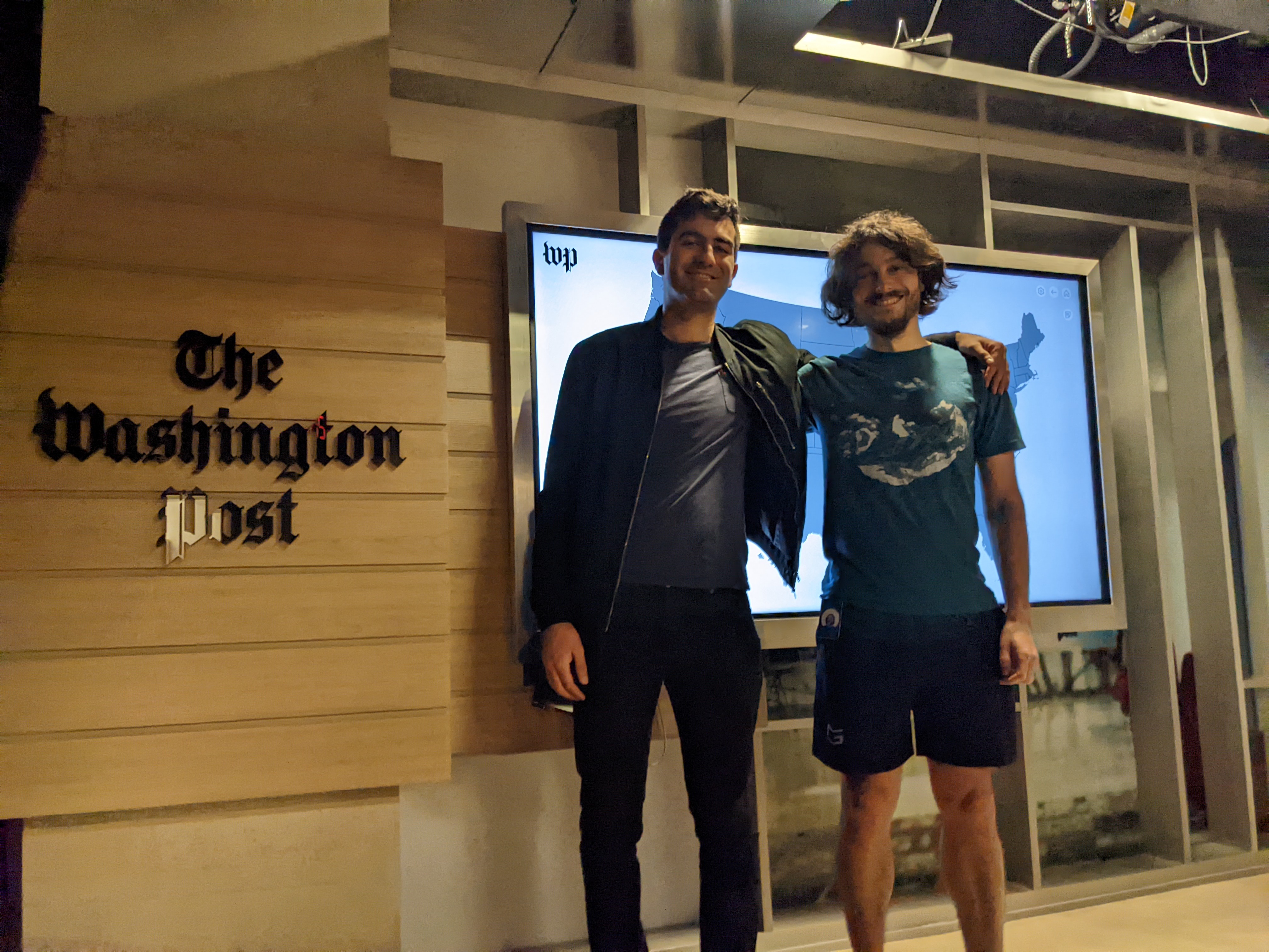 Alex Petros and Dylan Freedman in front of a big screen with a gray map on it,
       at the Washington Post offices